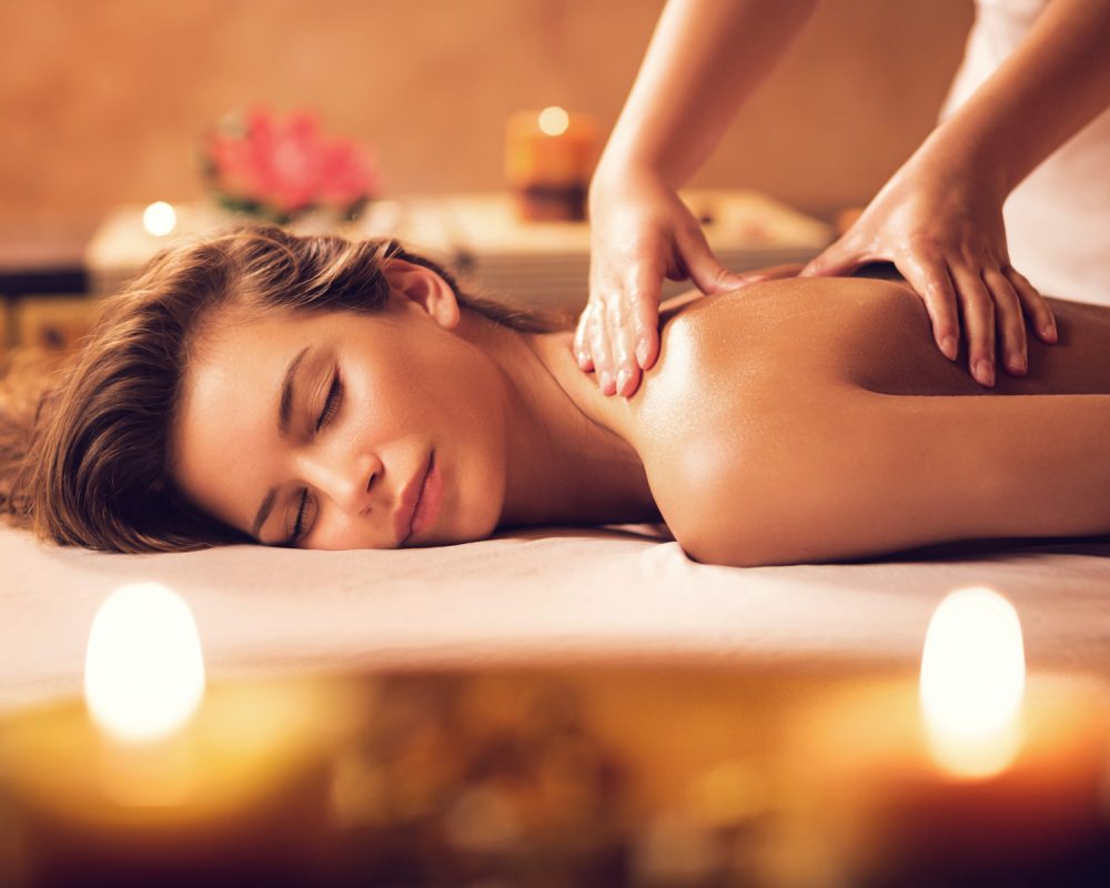 Young woman relaxing during back massage at the spa. Donna distesa su un lettino da massaggio, rilassata mentre riceve un trattamento alla schiena in un ambiente caldo e avvolgente, con candele e atmosfera zen tipica del centro estetico Invaien a Padova.